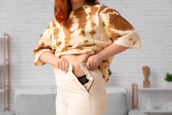 Image of woman trying to do her trousers up after pregnancy weight gain Sandy