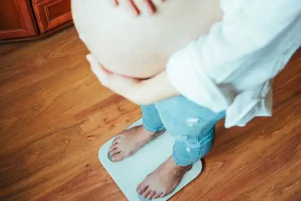 Image of woman weighing herself and experiencing weight gain through pregnancy Sandy